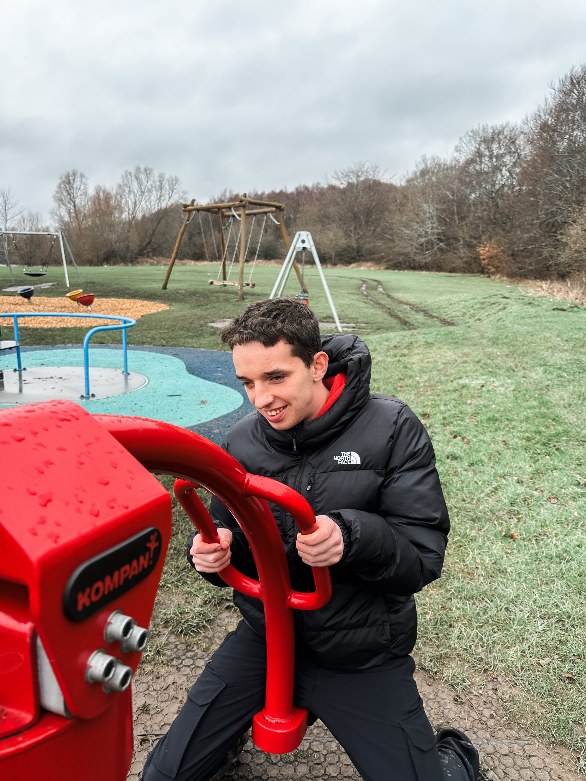A young man with additional support needs being supported in the community at a play area in a park